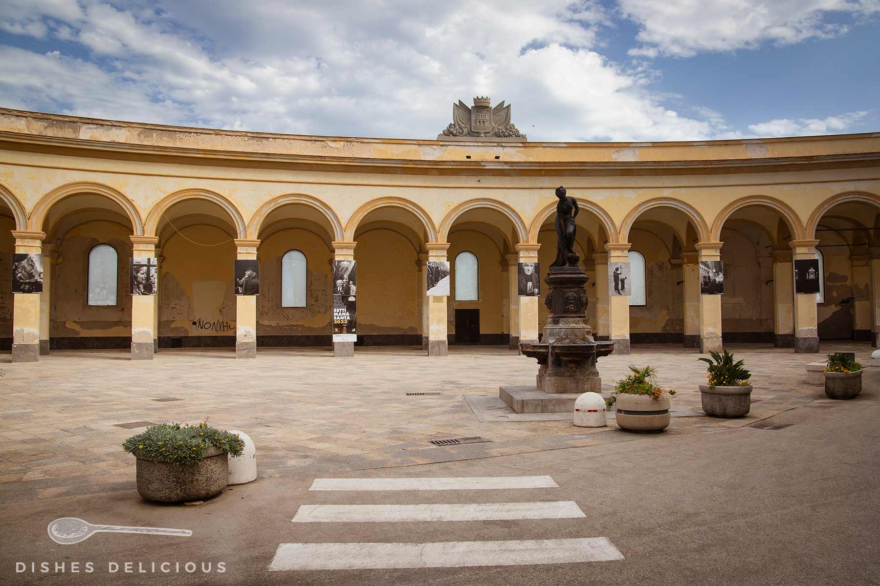 Der alte Mercato del Pesce: Arkadenhof mit beiger Fassade, mehreren Rundbögen, einer Statue auf einem Podest in der Mitte und Pflanzkübeln auf dem Boden.