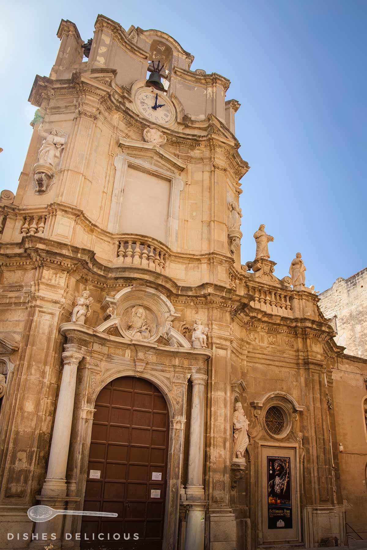 Barocke Fassade der Purgatorio-Kirche mit Uhr, Skulpturen und großem Holztor unter blauem Himmel.
