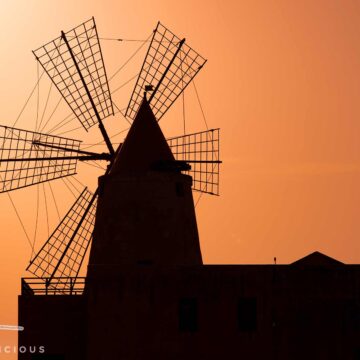 Saline Ettore e Infersa bei Trapani: Silhouette der Windmühle mit vier Flügeln vor orangefarbenem Himmel bei Sonnenuntergang.