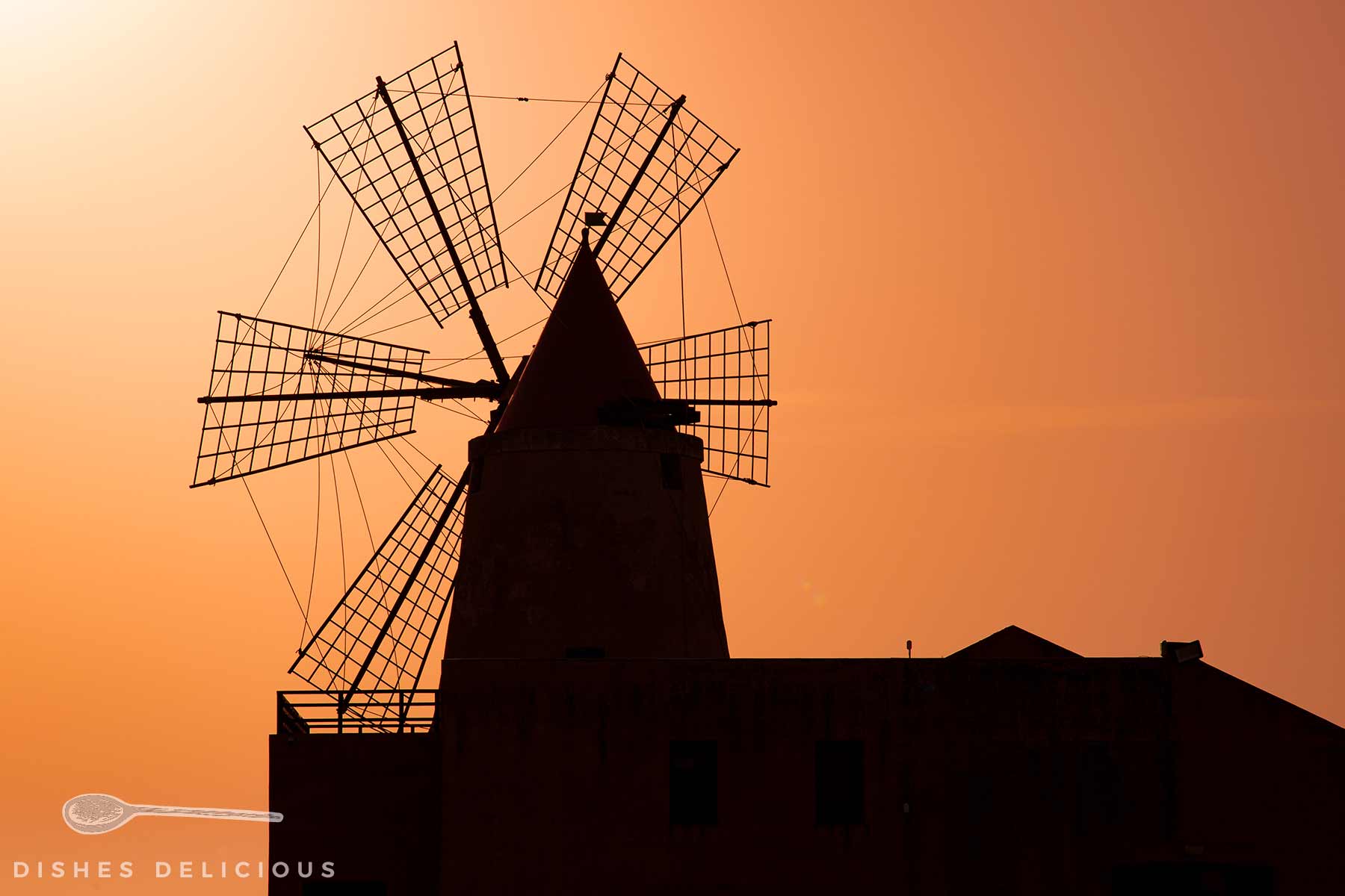 Saline Ettore e Infersa bei Trapani: Silhouette der Windmühle mit vier Flügeln vor orangefarbenem Himmel bei Sonnenuntergang.