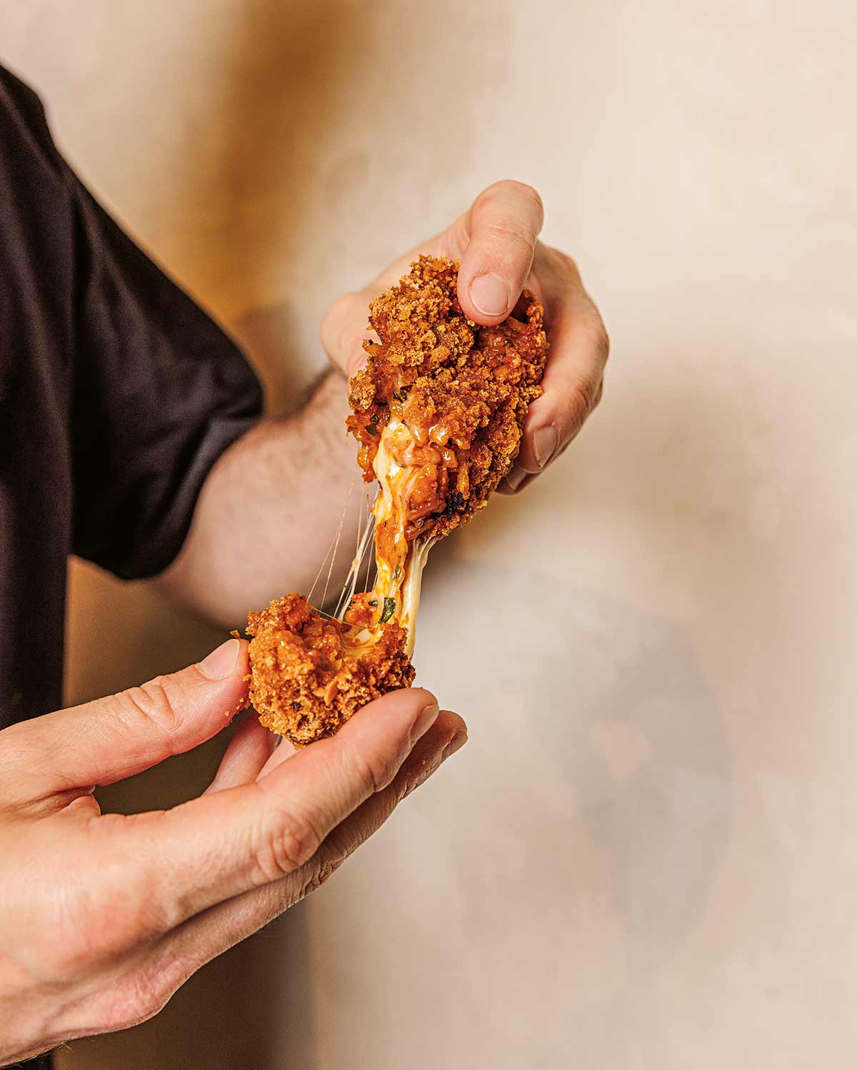 Zwei Hände ziehen eine knusprige, gefüllte Reiskrokette auseinander, aus dem geschmolzener Käse zieht.