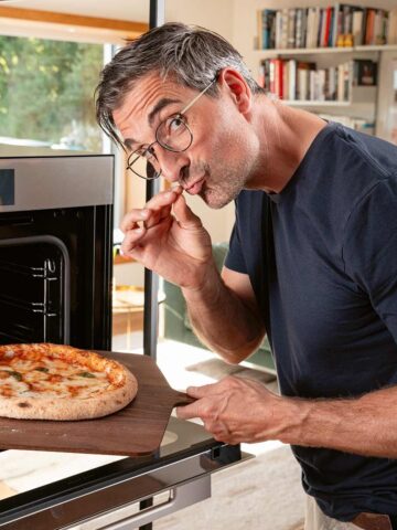 Hubertus Tzschirner steht am Backofen und holt mit einem Holzbrett eine Pizza aus dem Ofen.