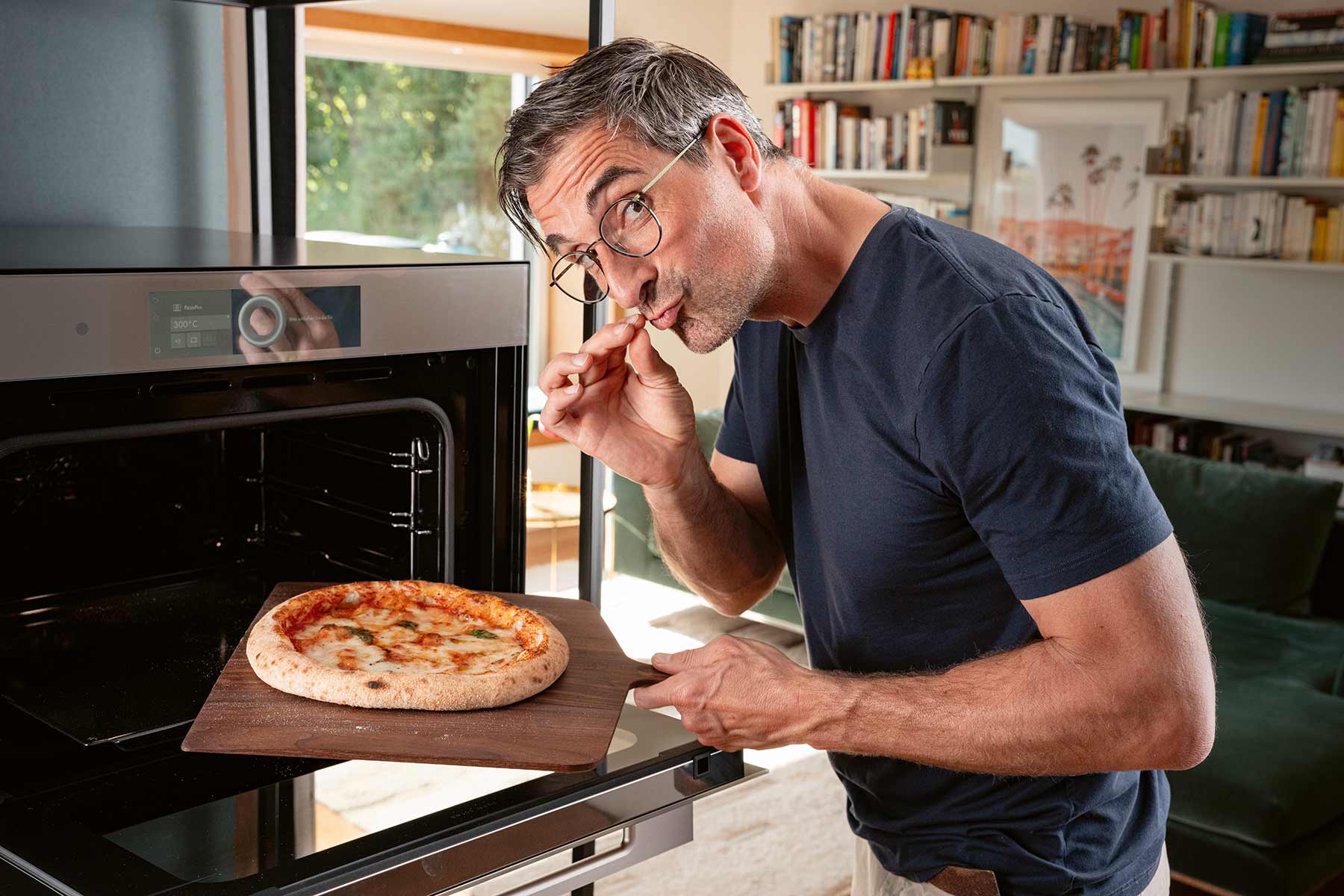 Hubertus Tzschirner steht am Backofen und holt mit einem Holzbrett eine Pizza aus dem Ofen.