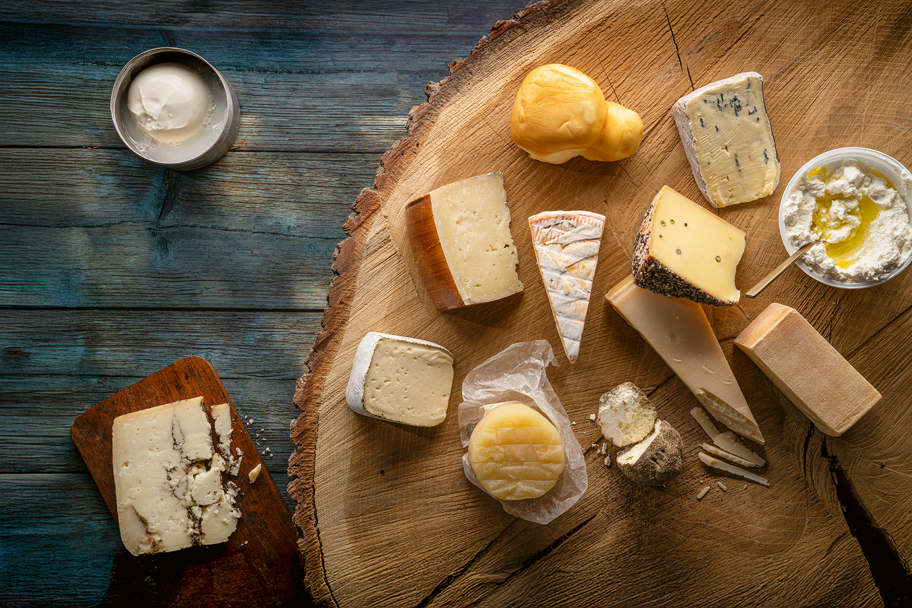 Verschiedene Käsesorten mit unterschiedlichen Formen und Rinden auf einem großen Holzbrett und einem kleinen Holzbrett.