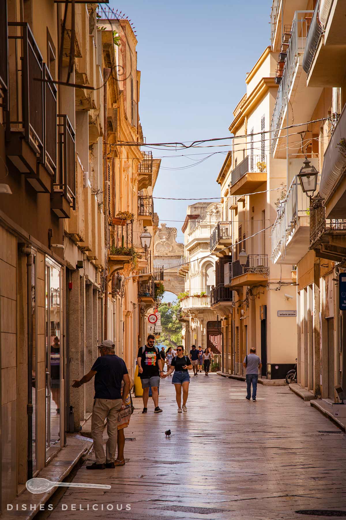 Eng bebaute Straße mit historischen Gebäuden in der Altstadt von Marsala, Passanten flanieren.