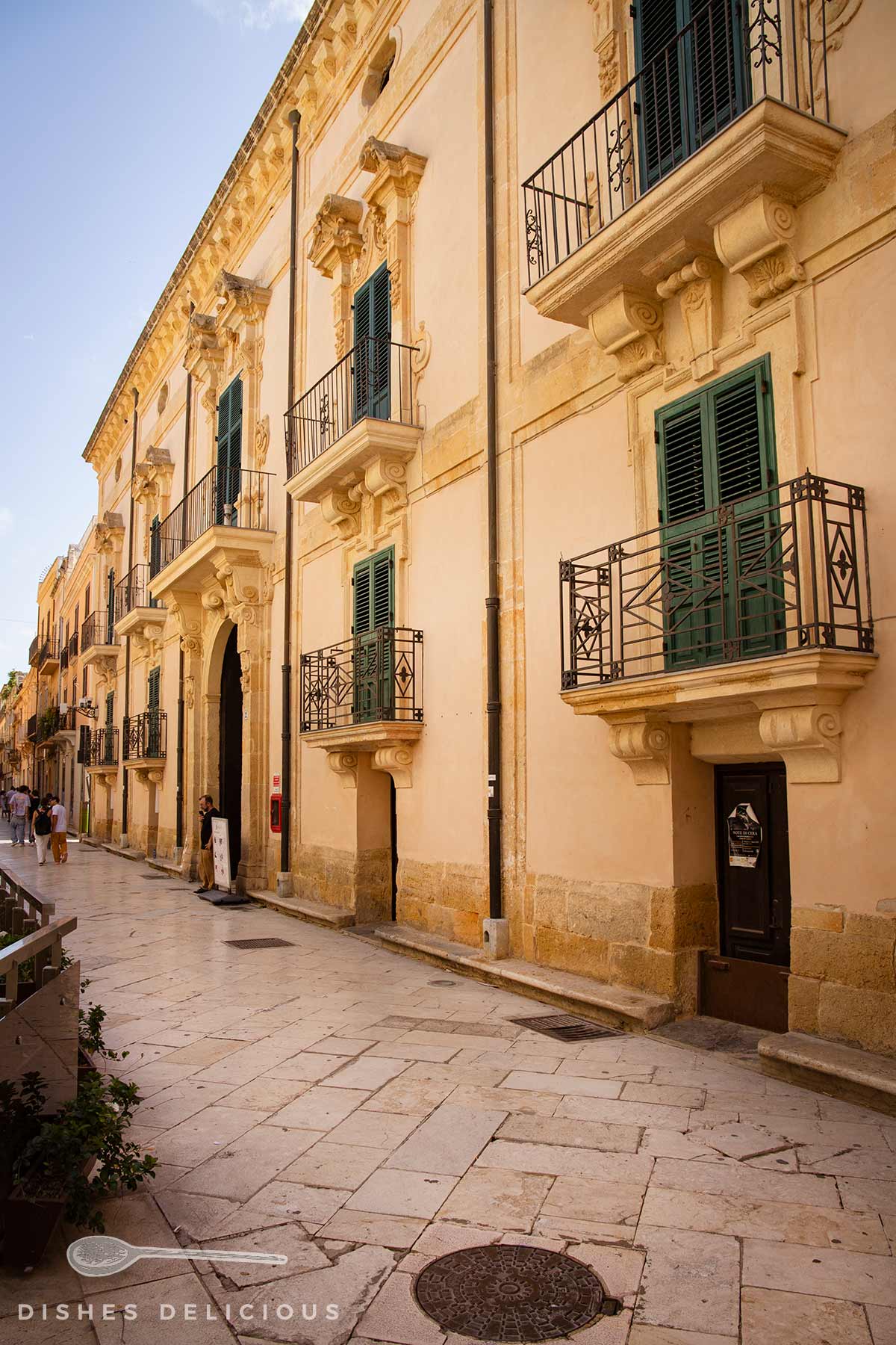 Palazzo Fici mit grünen Fensterläden und schmiedeeisernen Balkonen an gepflastertem Weg.