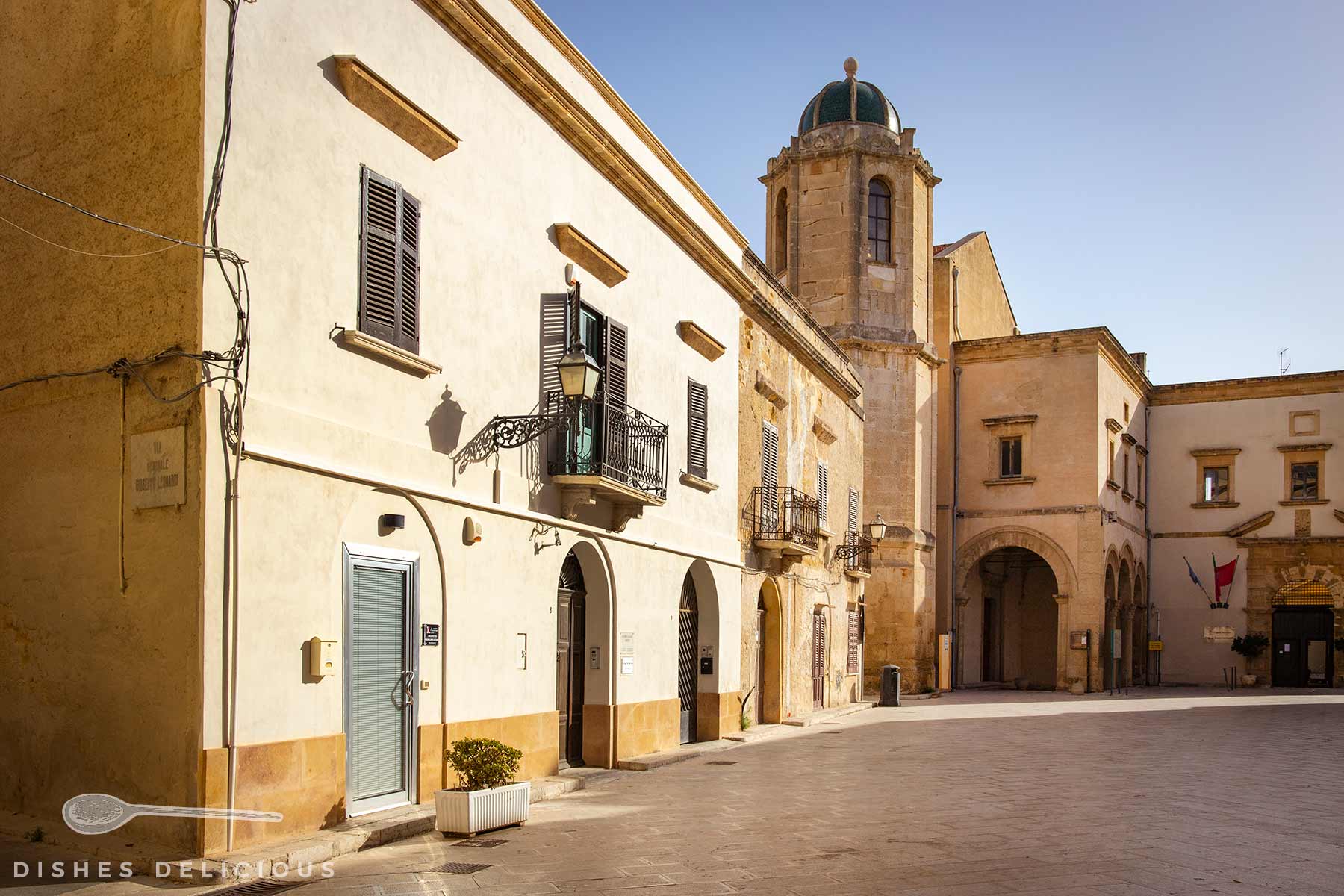 Torre Campanaria mit Säulengang, Rundbögen und einem Turm mit grünem Kuppeldach bei sonnigem Himmel.