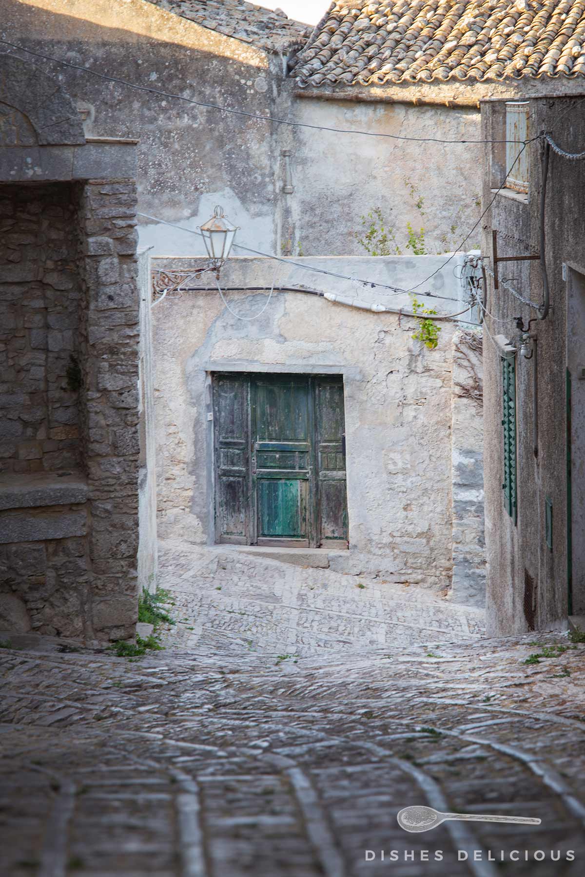 Verwitterte grüne Holztür in altem Steinbau an gepflastertem Weg.