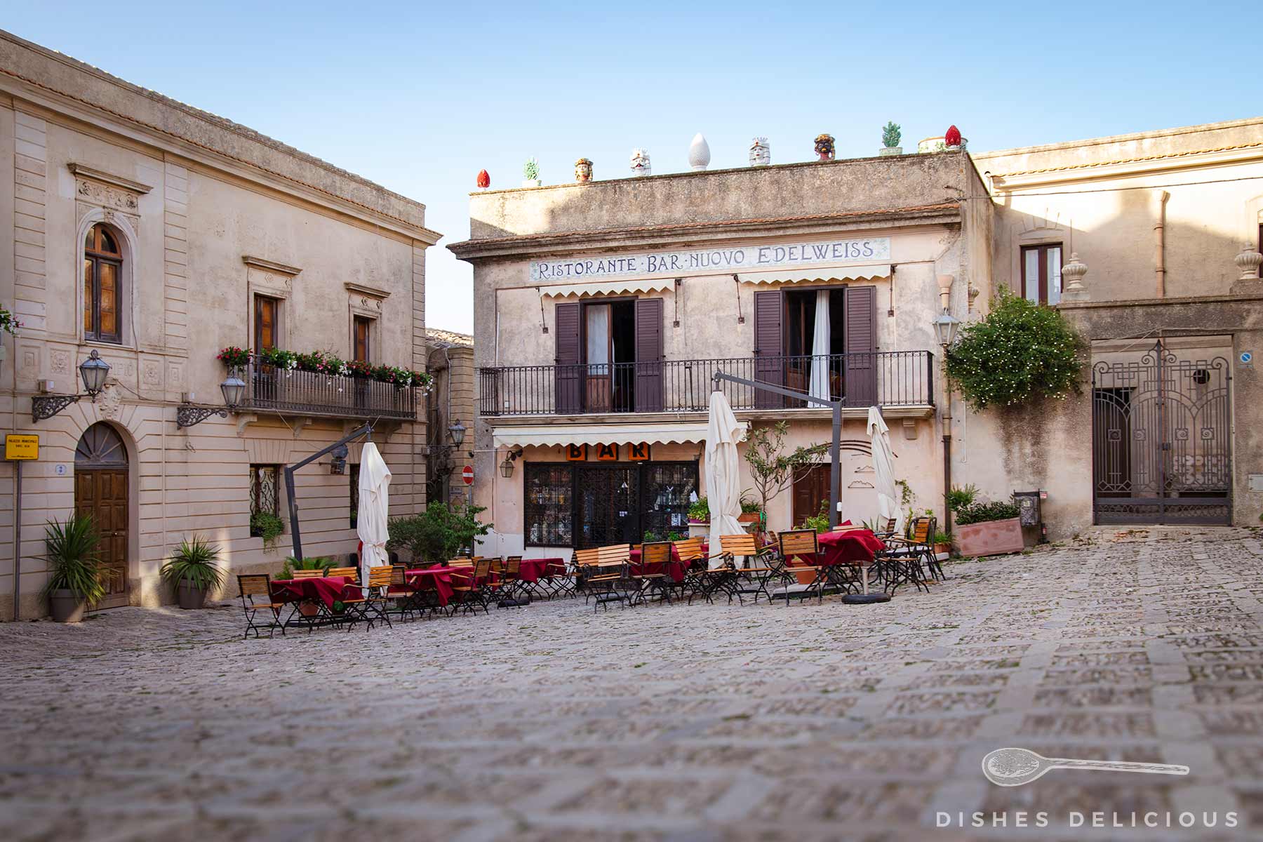 Gepflasterte Piazza della Loggia mit zwei Personen, umgeben von historischen Palazzi und einem Restaurant mit Markise und Außenbestuhlung.