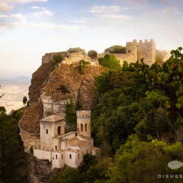 Torretta Pepoli: Kleines Schloss mit zwei Türmen auf steinigem Felsen, umgeben von dichtem Grün.