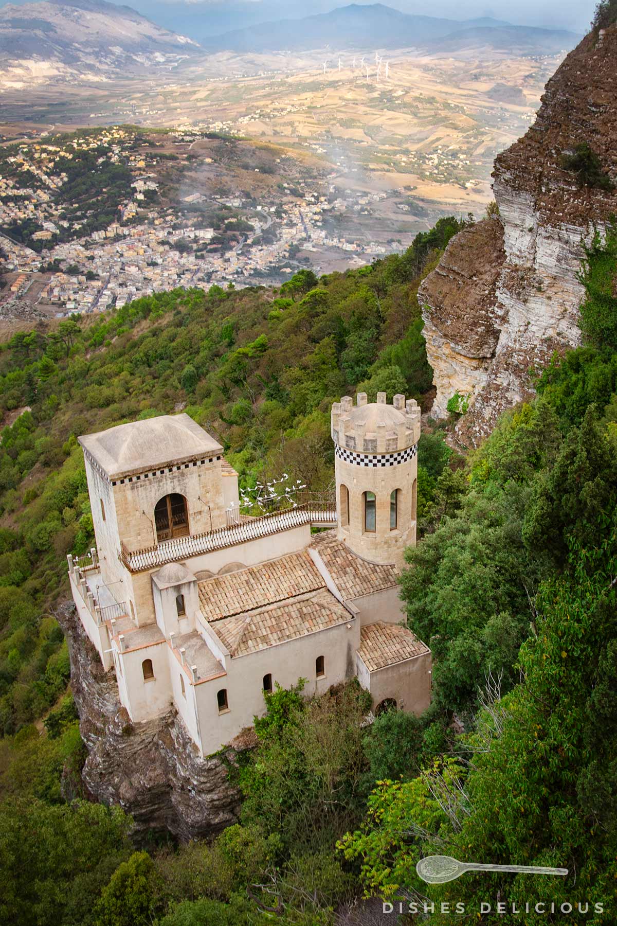 Torretta Pepoli in Erice mit rechteckigem und rundem Turm auf bewaldetem Felsen, im Hintergrund Tal mit Ortschaft und Bergen.