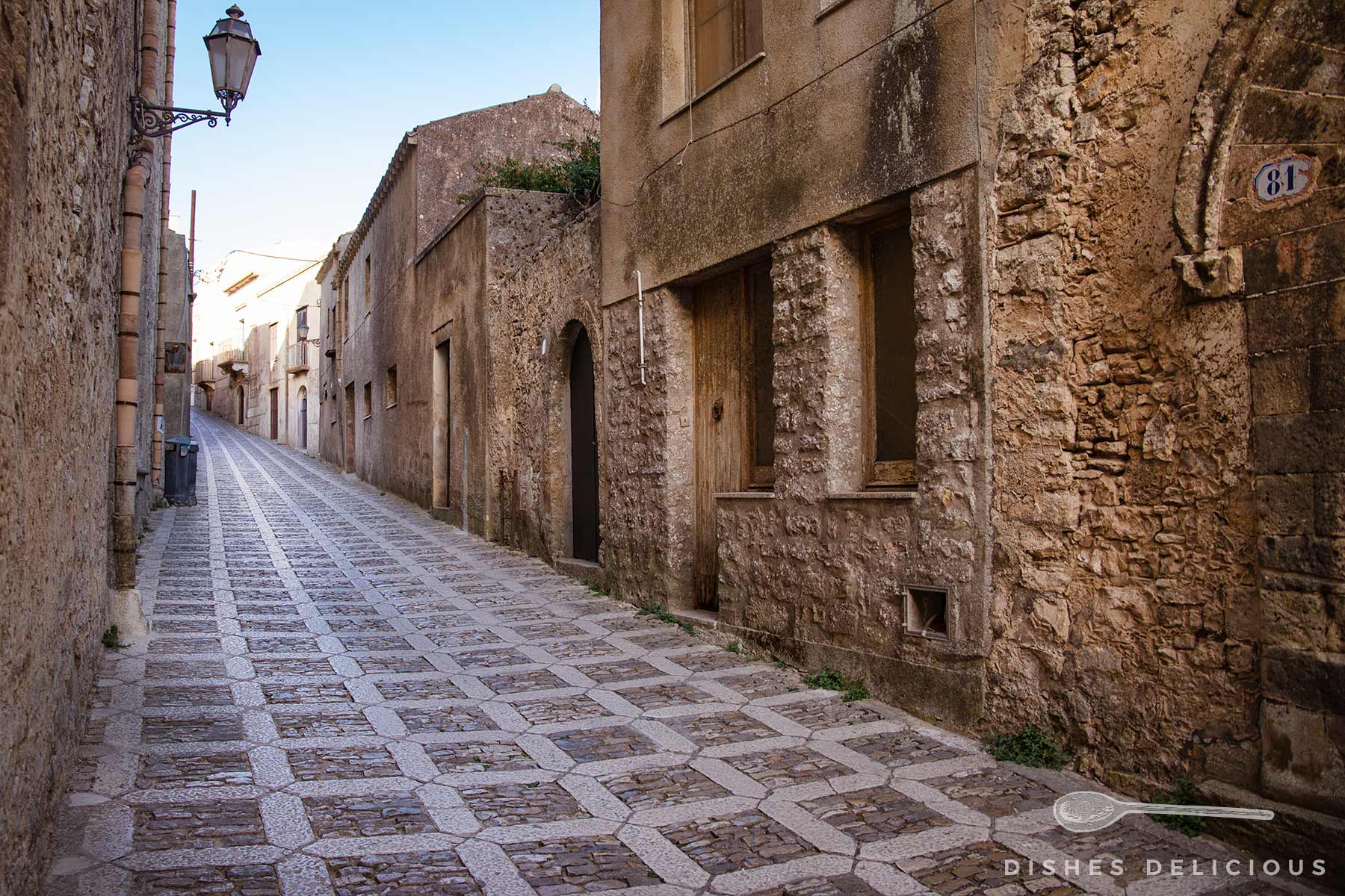 Via Vittorio Emanuele in Erice mit gepflastertem Boden und alten, verwitterten Häusern auf beiden Seiten.
