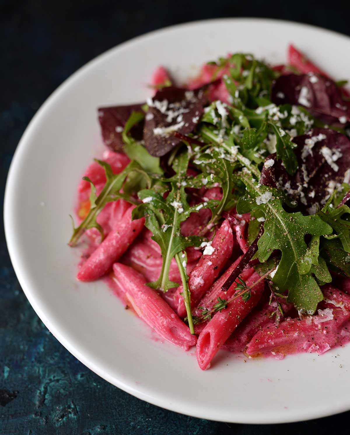 Teller mit Penne in roter-Bete-Creme, garniert mit Rucola und Blattsalat, bestreut mit geriebenem Käse,