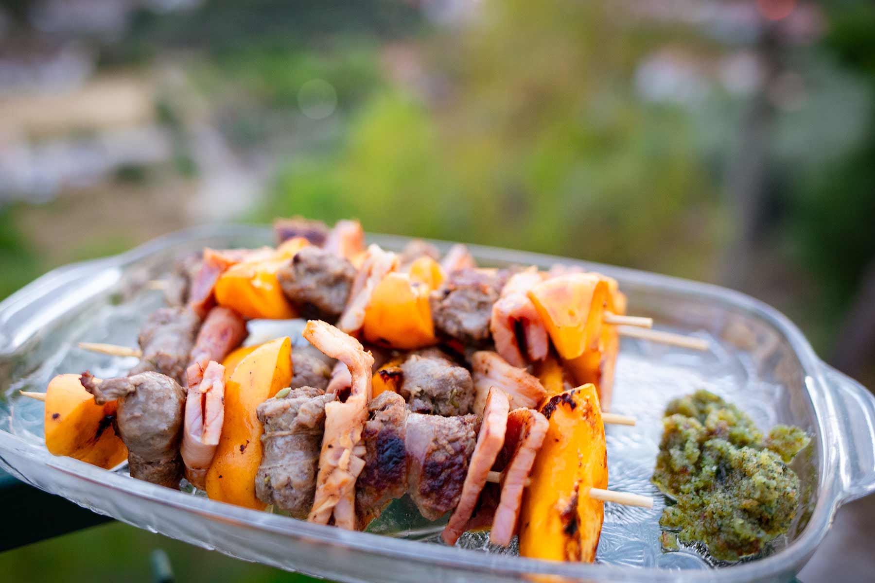 Servierteller mit Salsiccia-Schinken-Pfirsich-Spießen, daneben ein Minzpesto.