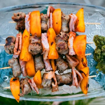 Servierplatte mit vier Grillspießen aus Salsiccia-Schinken-Pfirsich, daneben ein Minzpesto