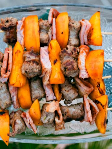 Servierplatte mit vier Grillspießen aus Salsiccia-Schinken-Pfirsich, daneben ein Minzpesto