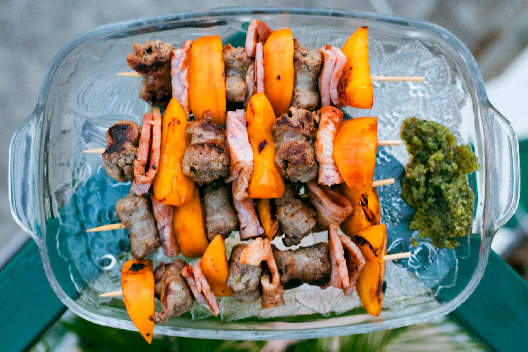 Servierplatte mit vier Grillspießen aus Salsiccia-Schinken-Pfirsich, daneben ein Minzpesto