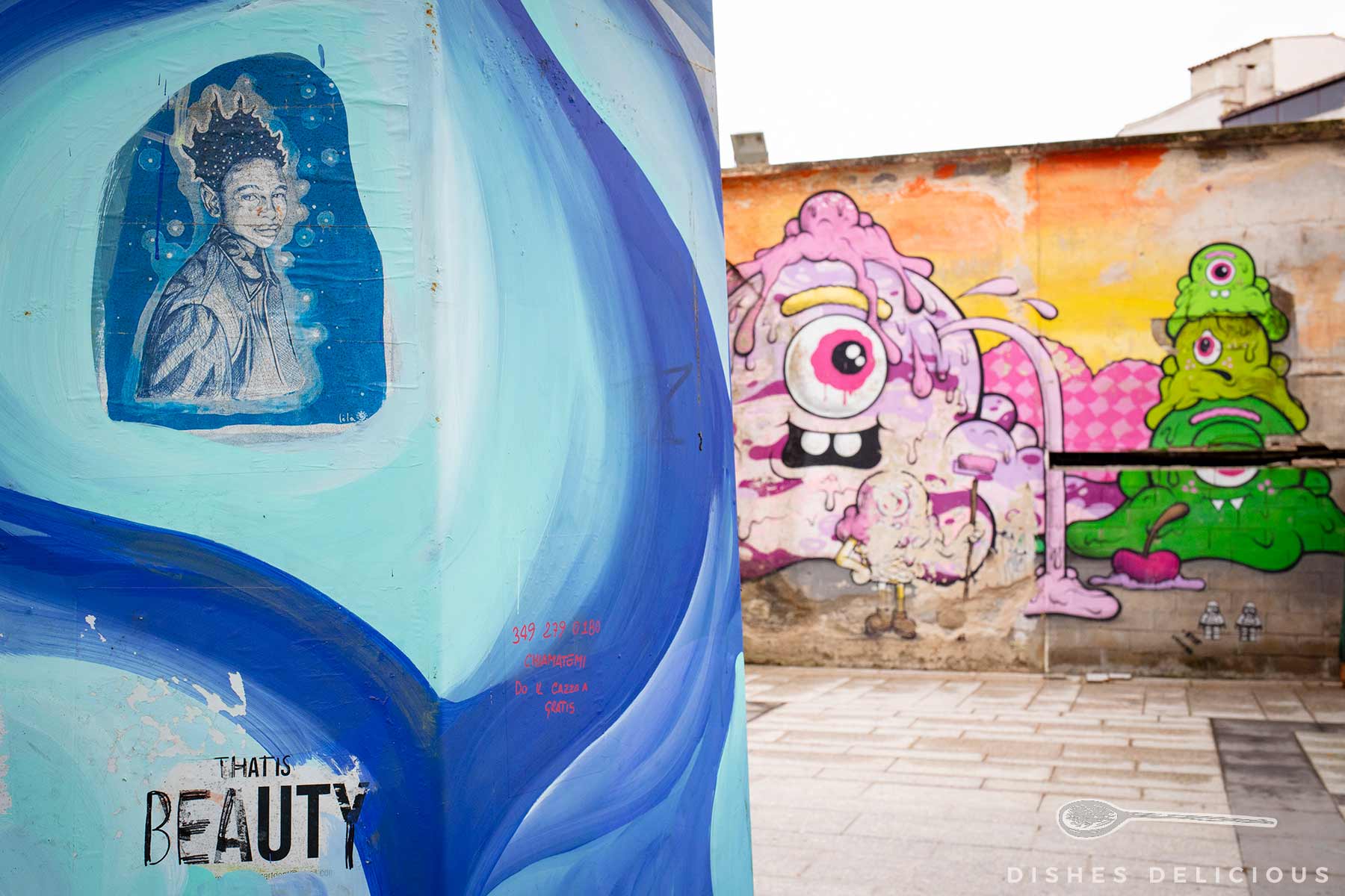 Straßengraffiti mit einem Porträt einer Frau und bunten, cartoonartigen Monstern auf Hauswänden in der Altstadt von Olbia.