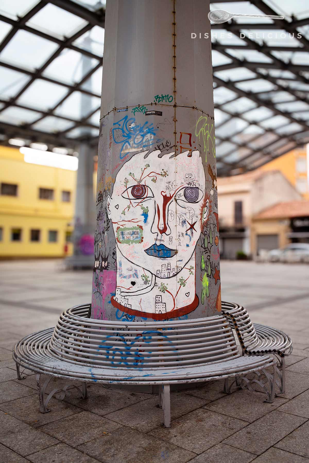 Graffiti eines stilisierten Gesichts mit blauen Lippen und roten Nasenlinien auf einer Säule in einem überdachten öffentlichen Raum.