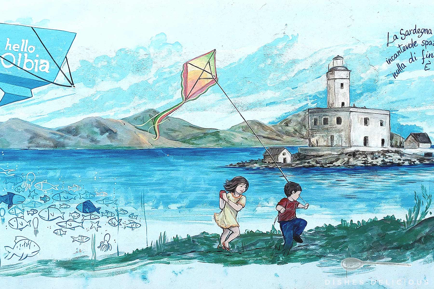 Wandmalerei in Olbia: Zwei Kinder spielen am Ufer mit einem Drachen vor einem Leuchtturm und Bergen im Hintergrund.