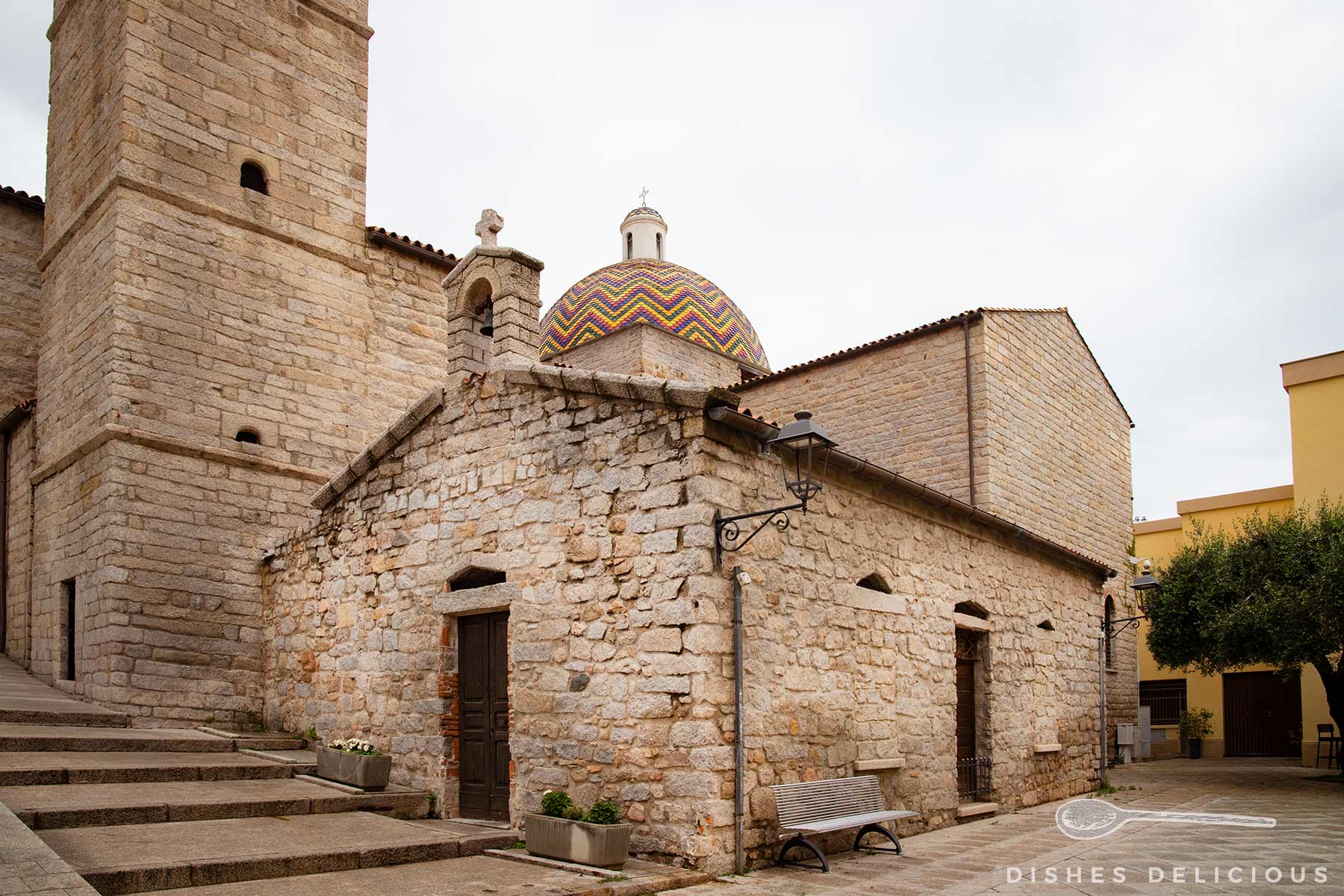 Steinerne Kirche San Paolo mit bunter Majolika-Kuppel, Treppe links und Sitzbank rechts vor der Kirche.