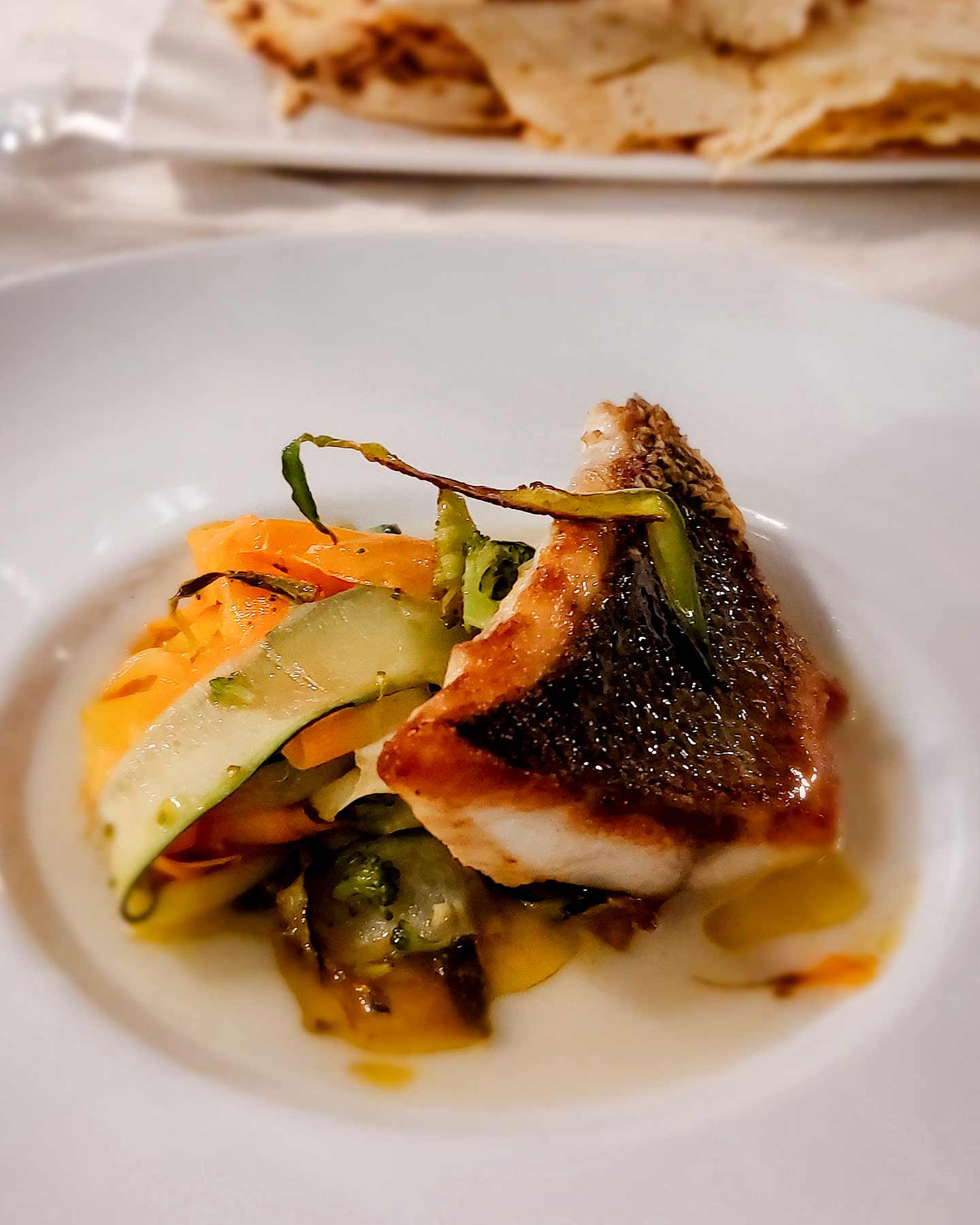 Gebratenes Fischfilet mit knuspriger Haut auf einem Bett aus dünn geschnittenem Gemüse auf weißem Teller.